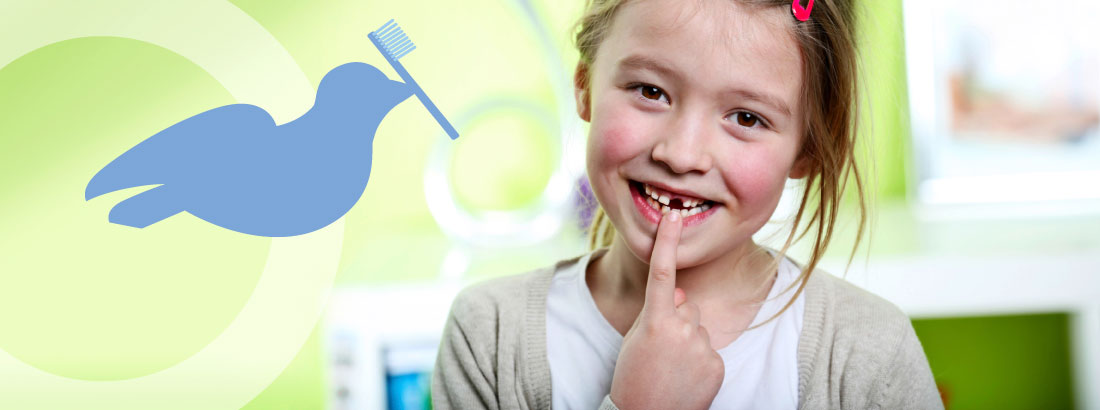Eine kleine Patientin in der Kinderzahnheilkunde-Behandlung, die auf ihre Zahnlücke zeigt, kombiniert mit dem Ulmer Spatz mit Zahnbürste im Schnabel.