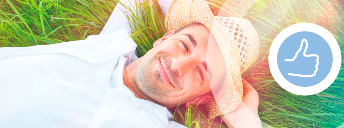 Ein sympathischer Mann mit Strohhut liegt lächelnd und entspannt im Gras nach einer schmerzfreien Zahnbehandlung.